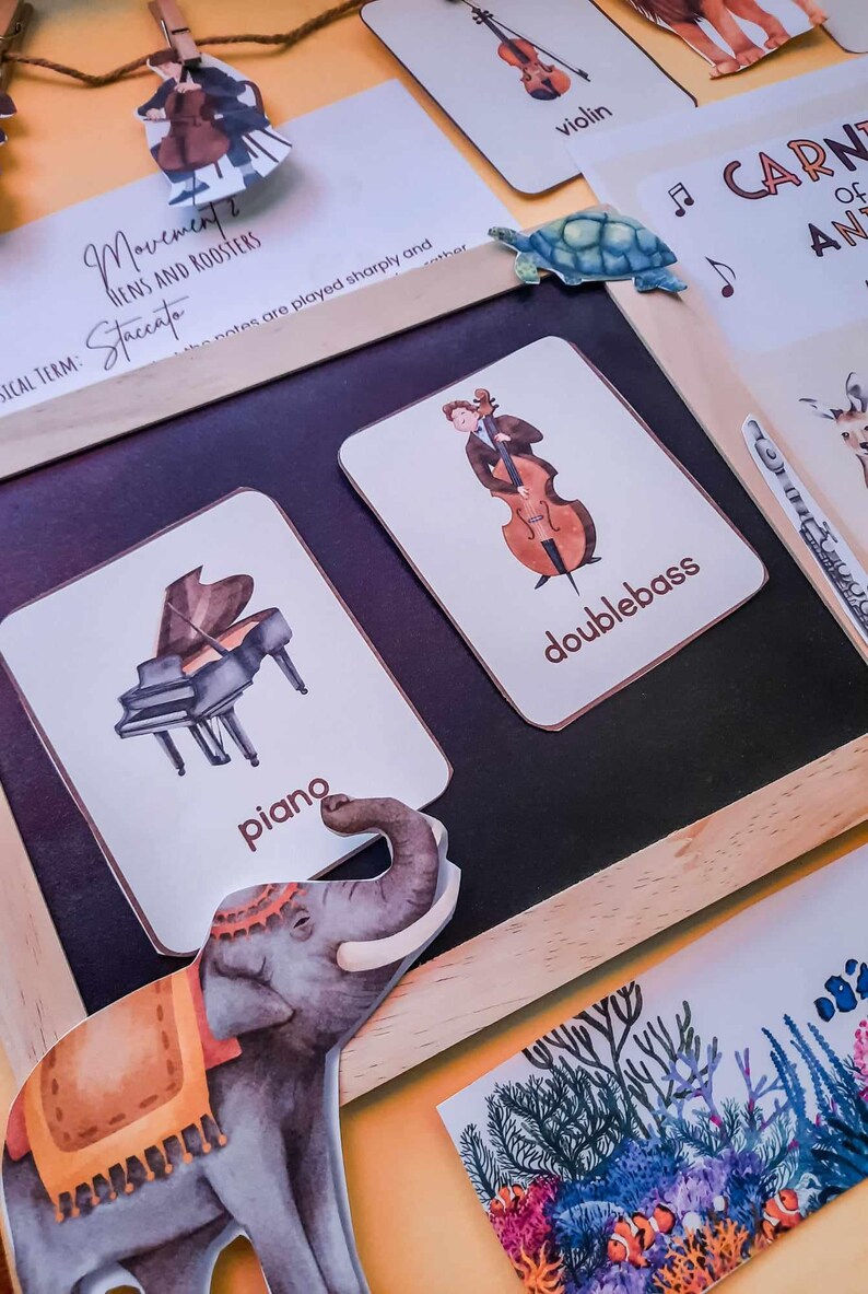 May include: A set of flashcards featuring illustrations of musical instruments, including a piano, double bass, and violin. The cards are on a chalkboard with a wooden frame. The text on the cards reads "piano", "double bass", and "violin".