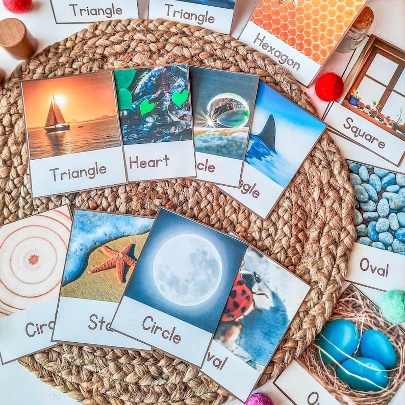Op de afbeelding: Educatieve flashcards met verschillende vormen en afbeeldingen, waaronder een zeilboot, zeester en lieveheersbeestje. De kaarten zijn gerangschikt op een geweven mat, met labels zoals "Driehoek", "Hart" en "Cirkel."