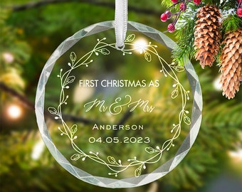 May include: Clear glass Christmas ornament with a white floral wreath design. The ornament reads "First Christmas as Mr & Mrs Anderson 04.05.2023".