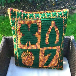 May include: A green, orange and yellow crocheted cushion with a shamrock, horseshoe, acorn and lightning bolt design.
