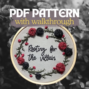 May include: An embroidery hoop with the text "Rooting for the Villain" in black thread. The design includes a floral wreath with red and black roses and the words "PDF PATTERN with walkthrough" at the top.