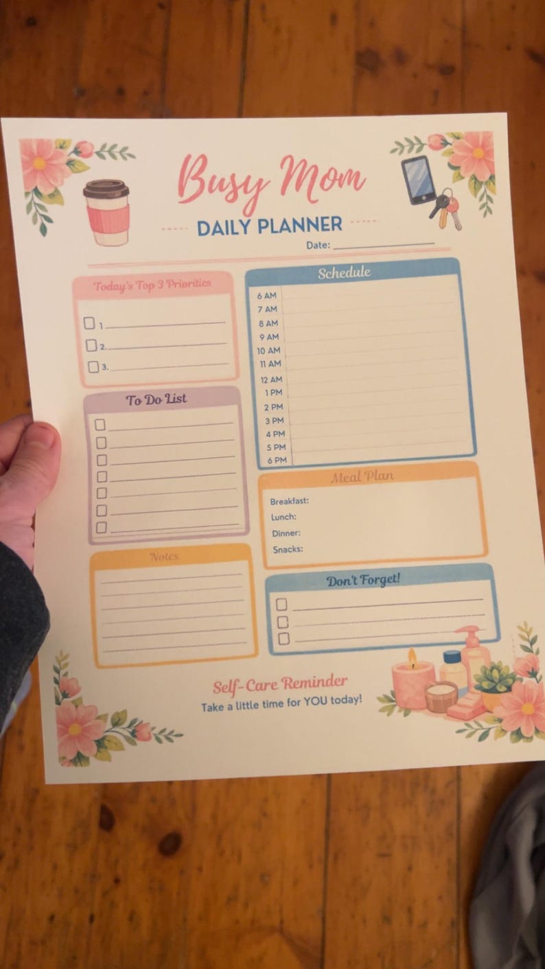May include: A printed daily planner titled "Busy Mom" with sections for priorities, to-do list, schedule, meal plan, notes, and reminders. The planner features floral and coffee cup illustrations, with the text "Self-Care Reminder" at the bottom.