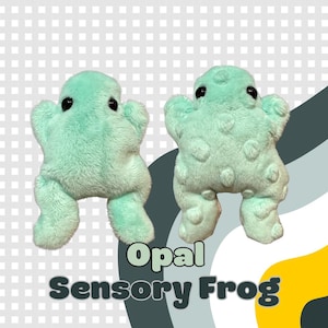 Puede incluir: Dos juguetes de peluche de rana verde menta con ojos negros. Las ranas tienen una superficie texturizada y afelpada y están en una pose juguetona. El texto "Opal Sensory Frog" se muestra en una fuente estilizada debajo.