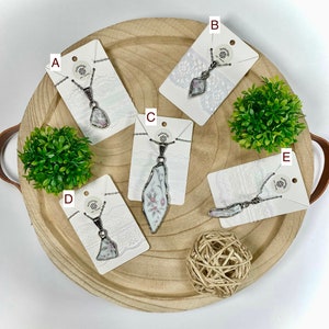 May include: Five necklaces with different porcelain pendants on white cards with lace trim. The pendants are all different shapes and feature floral patterns. The necklaces are displayed on a wooden tray.