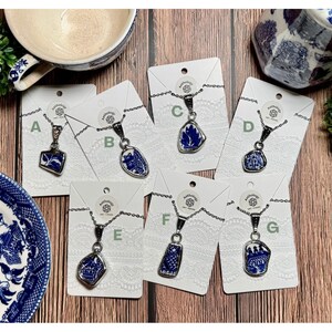 May include: Seven silver necklaces with blue and white porcelain pendants. Each pendant features a different design. The necklaces are displayed on white cards with the letters A through G.