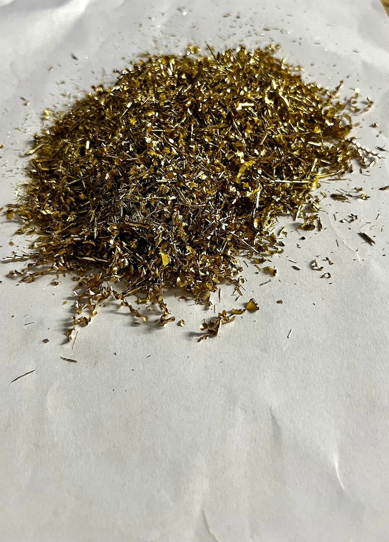 May include: A pile of gold-colored metal shavings on a white surface.