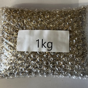 May include: A clear plastic bag filled with a large quantity of small, gold-colored metal pieces. The bag has a white label with the text "1 kg" printed on it.