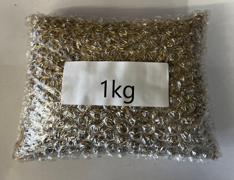 May include: A clear plastic bag filled with a large quantity of small, gold-colored metal pieces. The bag has a white label with the text "1 kg" printed on it.