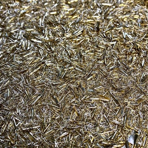 May include: A close-up of a surface covered in a dense layer of shimmering gold glitter. The glitter is made up of small, thin, and elongated pieces, creating a sparkling and reflective effect.