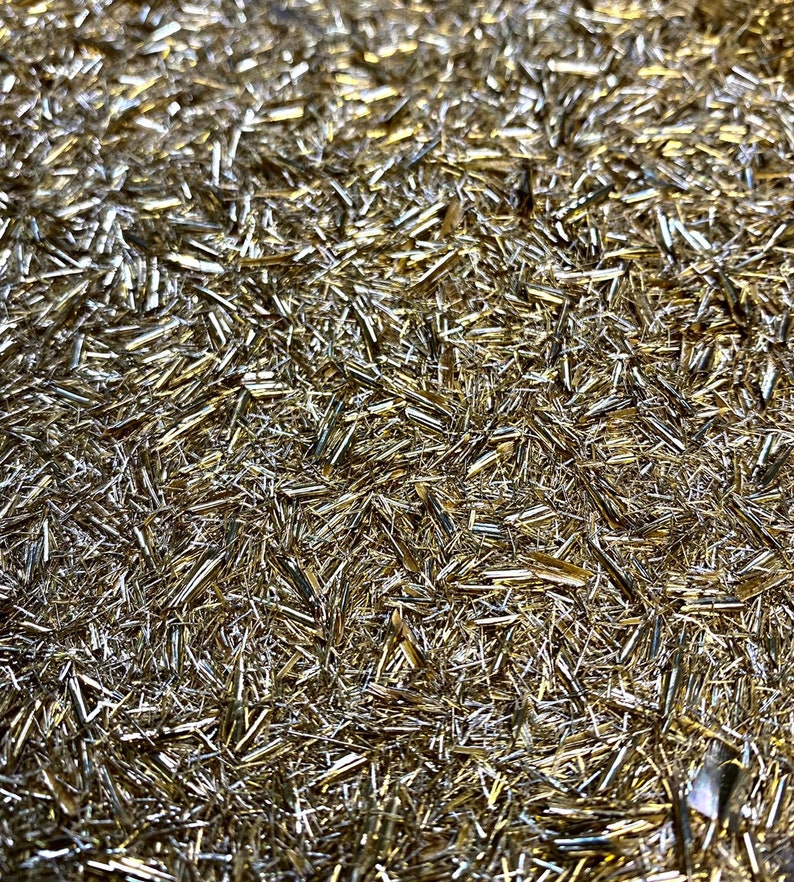 May include: A close-up of a surface covered in a dense layer of shimmering gold glitter. The glitter is made up of small, thin, and elongated pieces, creating a sparkling and reflective effect.