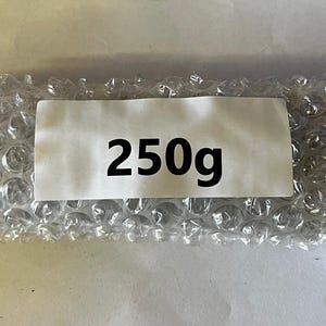 以下が含まれることがあります： 白いラベルに黒い文字で「250g」と印刷された、プチプチで包まれたパッケージです。