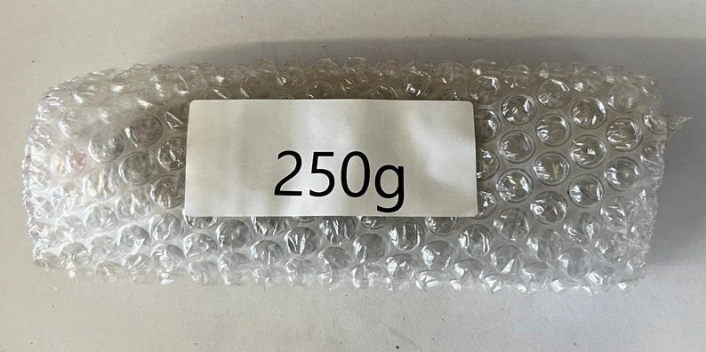 May include: A white bubble wrap package with a white label that says "250g".