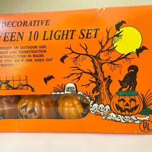 May include: Orange Halloween 10 Light Set box with a spooky illustration. The box features a jack-o'-lantern, black cat, bats, and a tree. The set includes pumpkin-shaped lights. The text on the box says "Decorative Halloween 10 Light Set".