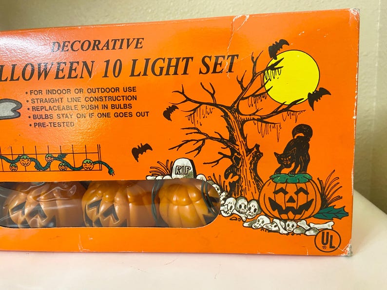 May include: Orange Halloween 10 Light Set box with a spooky illustration. The box features a jack-o'-lantern, black cat, bats, and a tree. The set includes pumpkin-shaped lights. The text on the box says "Decorative Halloween 10 Light Set".