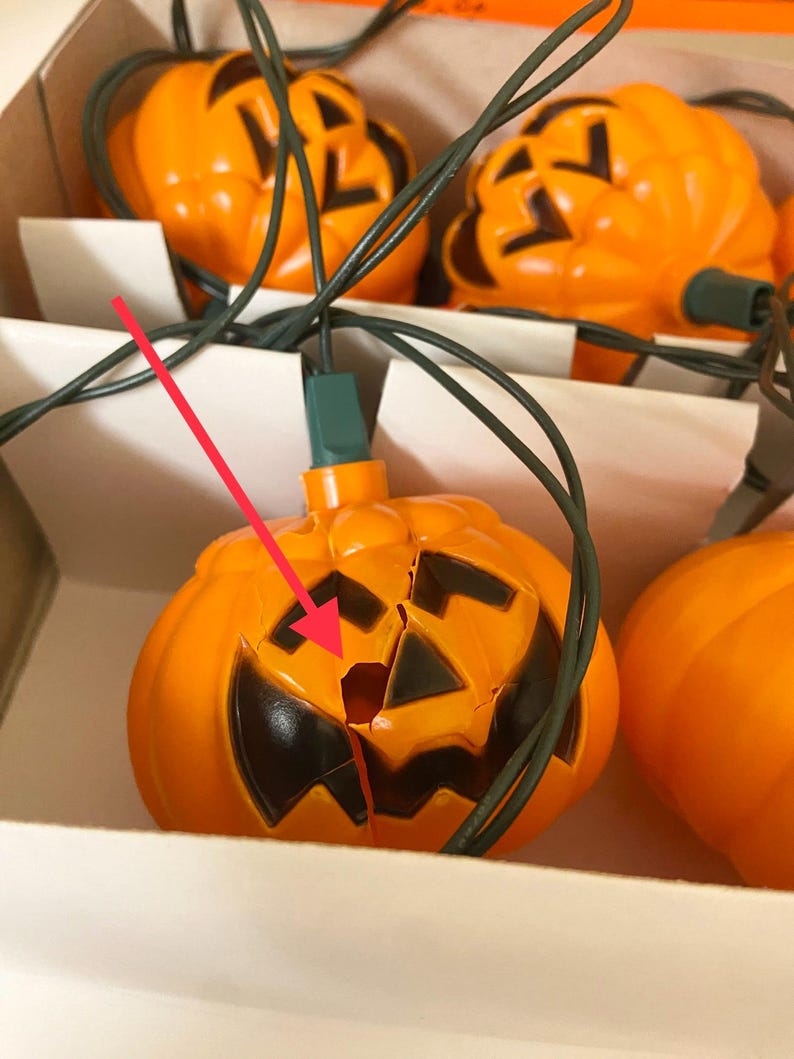May include: A string of orange jack-o'-lantern lights with black facial features. The lights are connected by green wires and are in a cardboard box. One pumpkin has a crack in it.