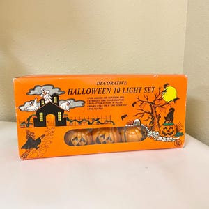 May include: An orange box with the text "DECORATIVE HALLOWEEN 10 LIGHT SET" features a Halloween-themed illustration. The illustration includes a haunted house, ghosts, a witch, and jack-o'-lantern lights. The box contains pumpkin-shaped lights.