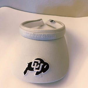 May include: White visor with a black and white University of Colorado buffalo logo and the text "University of Colorado" embroidered on the front.