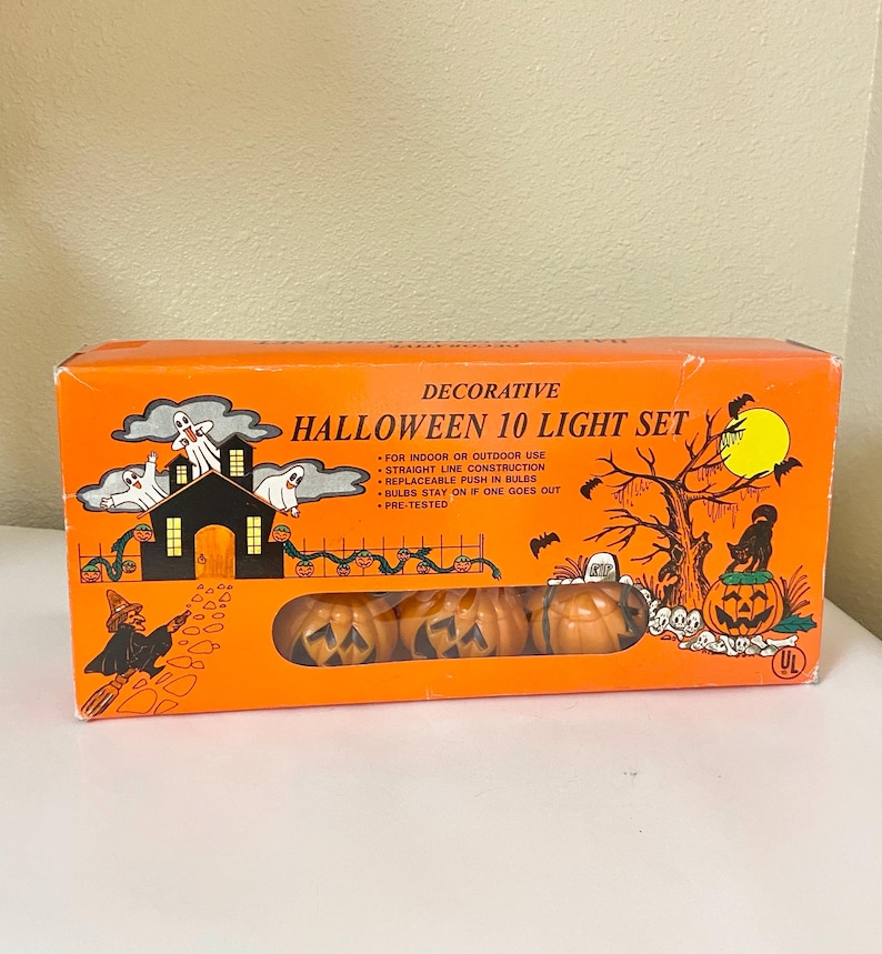 May include: Decorative Halloween 10 light set in an orange box. The box features illustrations of a haunted house, ghosts, a witch, and jack-o'-lanterns. The set includes pumpkin-shaped lights.