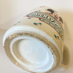 Pode incluir: Caneca de cer&acirc;mica branca com um design do Mickey Mouse Club. A caneca apresenta uma imagem de desenho animado do Mickey Mouse com notas musicais e as palavras "Mickey Mouse Club".