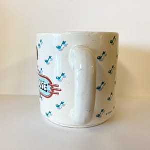 Pode incluir: Caneca de cer&acirc;mica branca com um design azul e vermelho com notas musicais e o texto "Mickey's House".