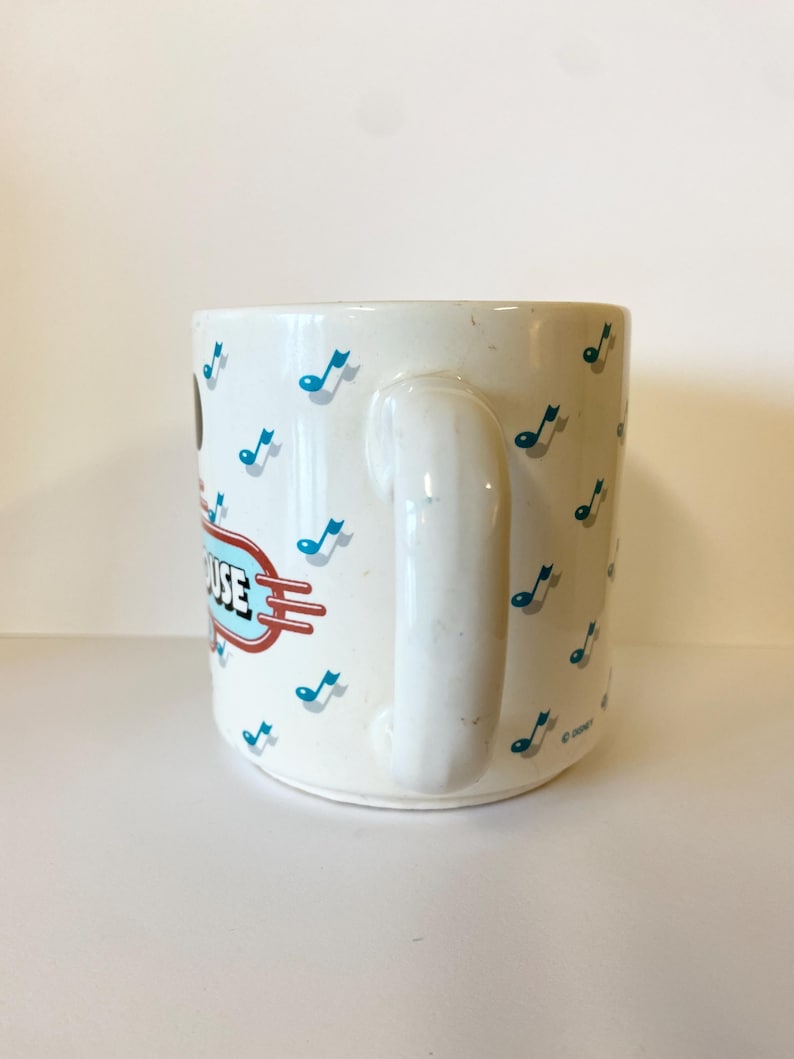 Pode incluir: Caneca de cer&acirc;mica branca com um design azul e vermelho com notas musicais e o texto "Mickey's House".