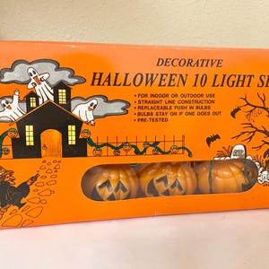 May include: Orange box with a Halloween 10 Light Set. The box features illustrations of ghosts, a haunted house, pumpkins, and a witch. The set includes pumpkin-shaped lights. Text on the box reads "Decorative Halloween 10 Light Set."