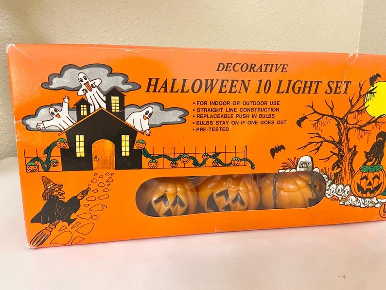 May include: Orange box with a Halloween 10 Light Set. The box features illustrations of ghosts, a haunted house, pumpkins, and a witch. The set includes pumpkin-shaped lights. Text on the box reads "Decorative Halloween 10 Light Set."
