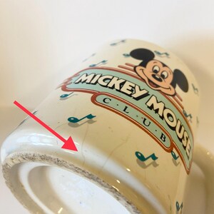 Pode incluir: Caneca de cer&acirc;mica branca com um design do Mickey Mouse Club. A caneca tem um esquema de cores azul e verde com notas musicais e as palavras "Mickey Mouse Club" impressas no lado. O fundo da caneca tem um pequeno lascado.