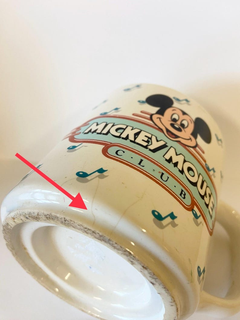 Pode incluir: Caneca de cer&acirc;mica branca com um design do Mickey Mouse Club. A caneca tem um esquema de cores azul e verde com notas musicais e as palavras "Mickey Mouse Club" impressas no lado. O fundo da caneca tem um pequeno lascado.