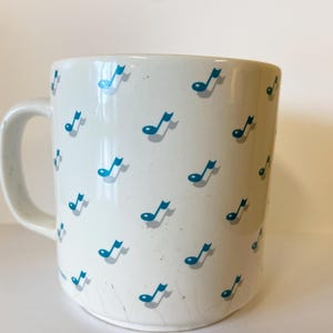 Pode incluir: Caneca de cer&acirc;mica branca com um padr&atilde;o de notas musicais azuis.