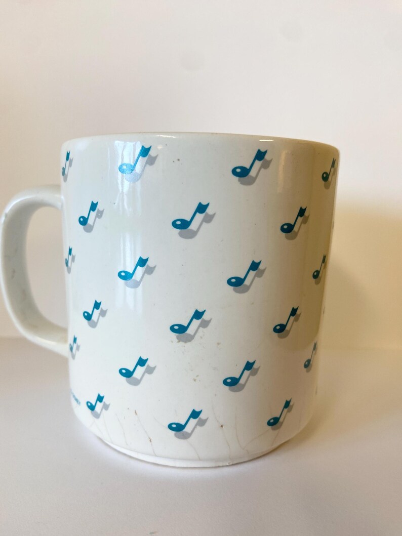 Pode incluir: Caneca de cer&acirc;mica branca com um padr&atilde;o de notas musicais azuis.