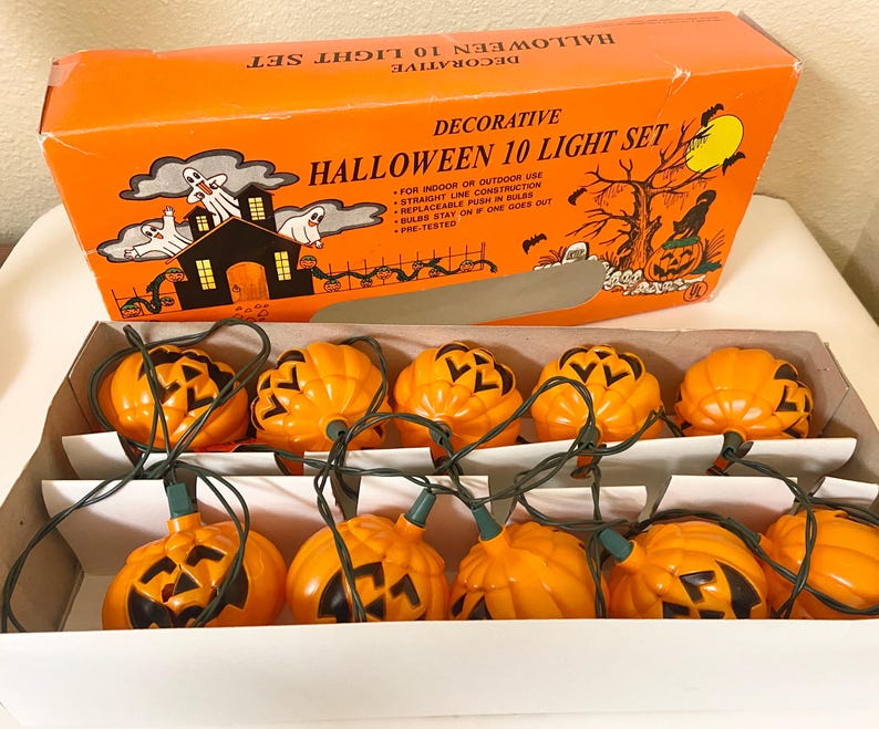 May include: An orange box labeled "Decorative Halloween 10 Light Set" with a string of orange pumpkin lights. The box features Halloween-themed illustrations of a haunted house, ghosts, and a jack-o'-lantern. The lights are in a white cardboard tray.