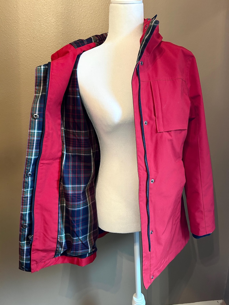 Puede incluir: Chaqueta rosa brillante con cremallera y ribetes azul marino. El interior de la chaqueta est&aacute; forrado con un estampado de cuadros en azul, verde y rojo. Tiene cuello alto y dos bolsillos delanteros. La chaqueta se exhibe en un maniqu&iacute;.