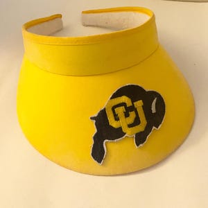 May include: Yellow visor with a black and gold University of Colorado Buffaloes logo patch.
