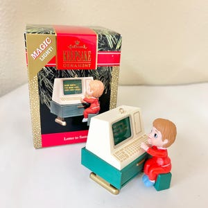 May include: Hallmark Keepsake Christmas ornament featuring a child in a red suit typing on a vintage computer. The computer is white and teal, with the text "Dear Santa, I've been very, very good!" on the screen. The box reads "Magic Light!" and "Letter to Santa."