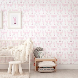 Puede incluir: Una habitación de bebé con papel tapiz de llamas rosa y blanco. La habitación cuenta con una cuna con una manta blanca, un taburete blanco y una estantería de madera con una almohada gris y blanca y un letrero de madera que dice "Bebé".