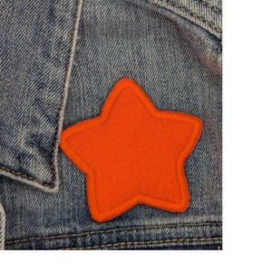 Puede incluir: Un parche en forma de estrella de color naranja brillante cosido en una chaqueta vaquera.