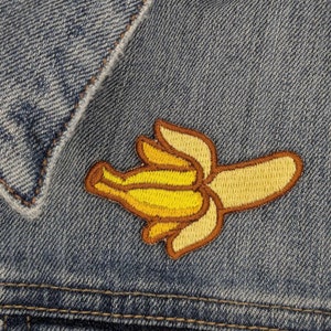 May include: A yellow and brown embroidered banana patch sewn onto a blue denim jacket.