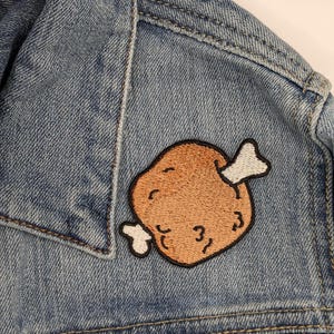 May include: A blue denim jacket with a brown embroidered patch of a chicken leg with a bone.