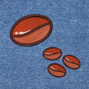 May include: Four brown embroidered coffee bean patches on a blue denim background. The largest bean is at the top and the three smaller beans are arranged in a triangle shape below it.