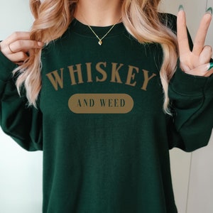 May include: A dark green sweatshirt with the text "WHISKEY AND WEED" printed in brown on the front.