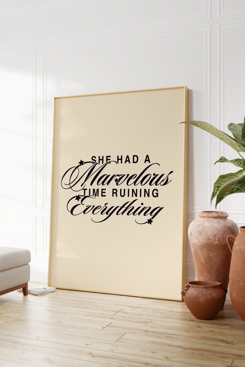 Op de afbeelding: Een beige ingelijste poster met zwarte tekst die "She had a marvelous time ruining everything" luidt. De poster hangt aan een witte muur met een plant in een pot en een houten vloer.
