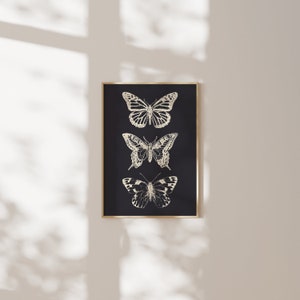 May include: A black framed print with three gold butterflies on a black background. The butterflies are arranged vertically, with the largest butterfly at the top and the smallest butterfly at the bottom.