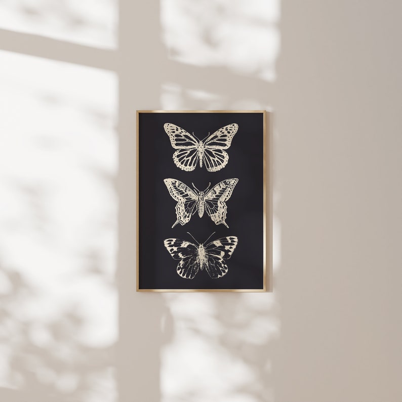 May include: A black framed print with three gold butterflies on a black background. The butterflies are arranged vertically, with the largest butterfly at the top and the smallest butterfly at the bottom.
