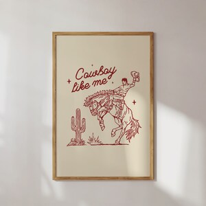 Może przedstawiać: Oprawiony wydruk z beżowym tłem przedstawia czerwony rysunek linii przedstawiający kowboja na koniu rodeo. Tekst "Cowboy like me" znajduje się nad ilustracją. Kaktus znajduje się po lewej stronie konia.