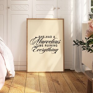 Op de afbeelding: Een ingelijst print met een witte achtergrond en zwarte tekst die "She had a marvelous time ruining everything" luidt. De print hangt aan een witte muur in een kamer met een bed en een plant.