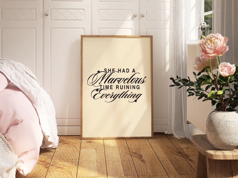 Op de afbeelding: Een ingelijst print met een witte achtergrond en zwarte tekst die "She had a marvelous time ruining everything" luidt. De print hangt aan een witte muur in een kamer met een bed en een plant.