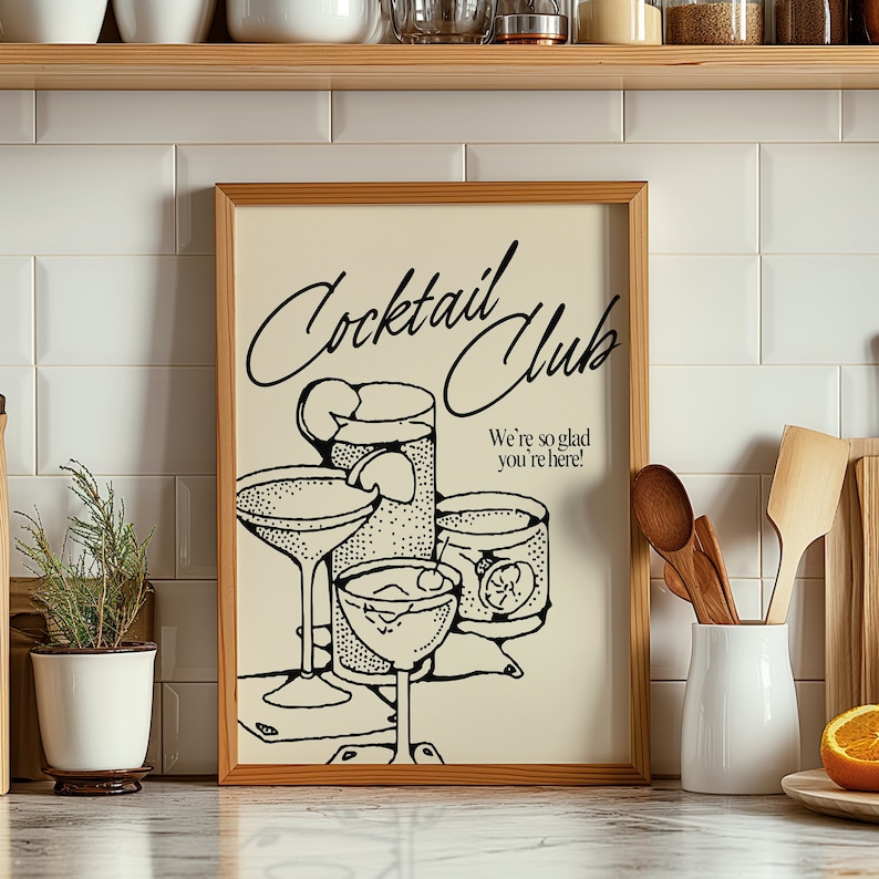 May include: A framed print with a vintage-style illustration of cocktail glasses. The print, in a light beige hue, features the words "Cocktail Club" in elegant script, along with the phrase "We're so glad you're here!" in a classic font. The artwork is set against a white tile background.