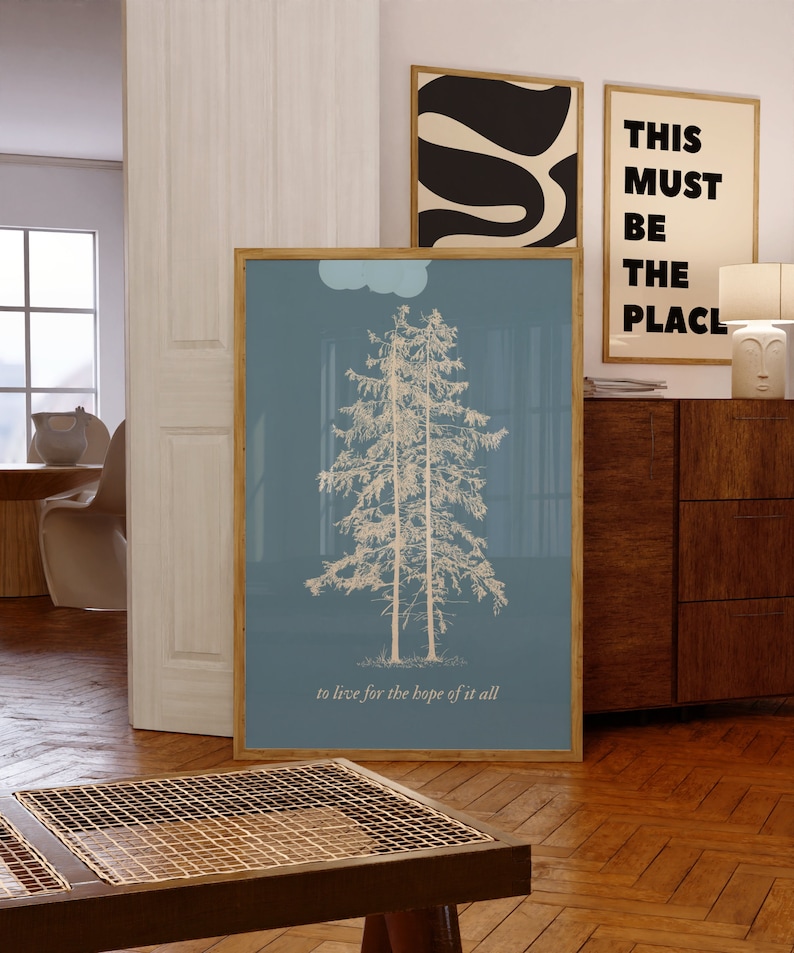 May include: A framed print with a blue background and a white outline of two pine trees. The text "to live for the hope of it all" is at the bottom of the print.