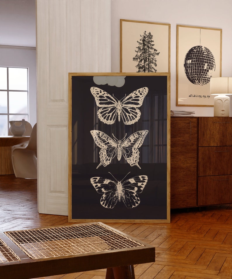 May include: A black framed print with three white silhouette butterflies on a dark blue background. The butterflies are arranged vertically, with the largest butterfly at the top and the smallest butterfly at the bottom.